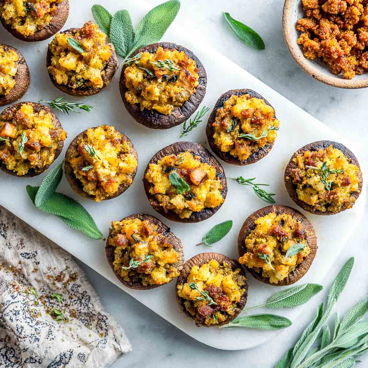 Baked mushroom caps stuffed with sausage and herbs, garnished with sage leaves.