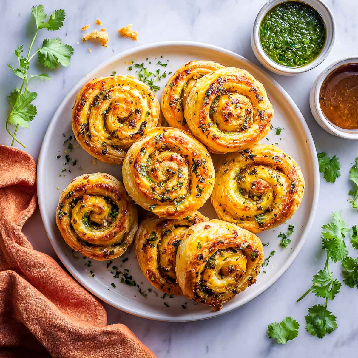 Masala pinwheel pastries on a white plate served with chutneys.