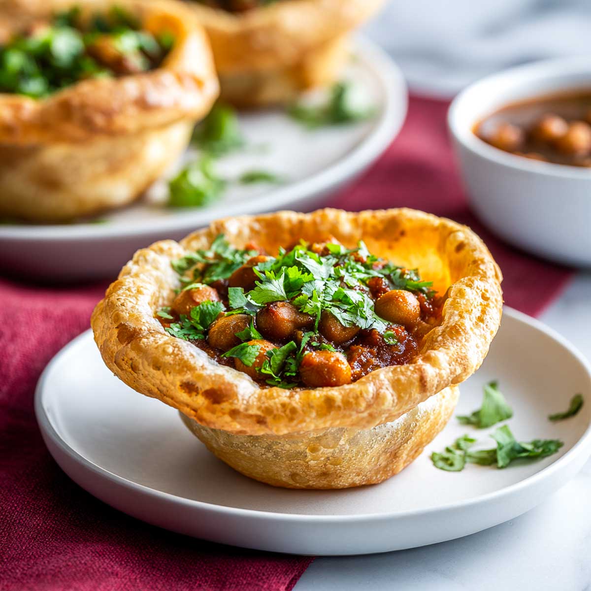 Small bhatura cups filled with spicy chickpea curry and served on a white plate.