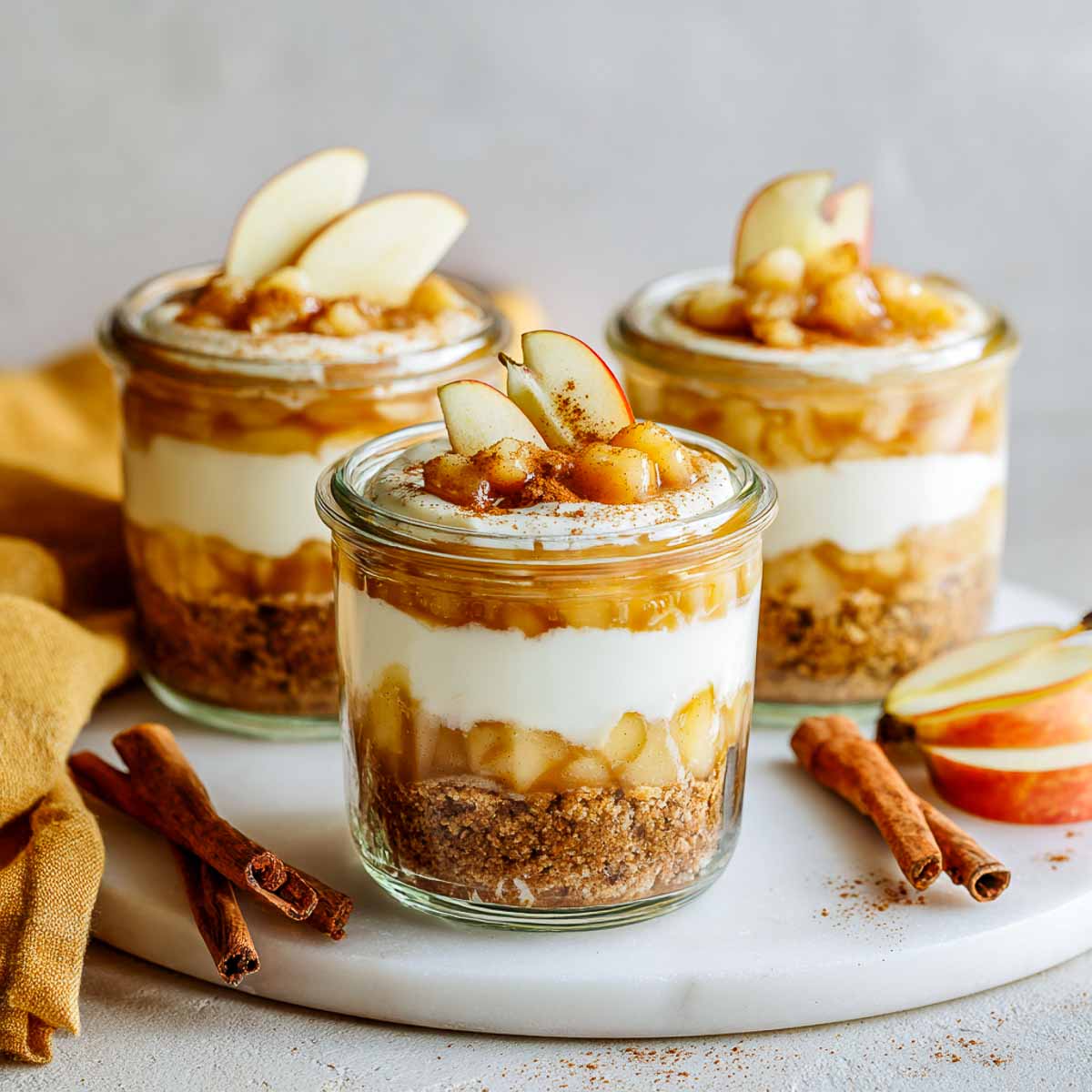Individual gluten-free apple cheesecake jars layered with cookie crust, creamy filling, and spiced apple topping.