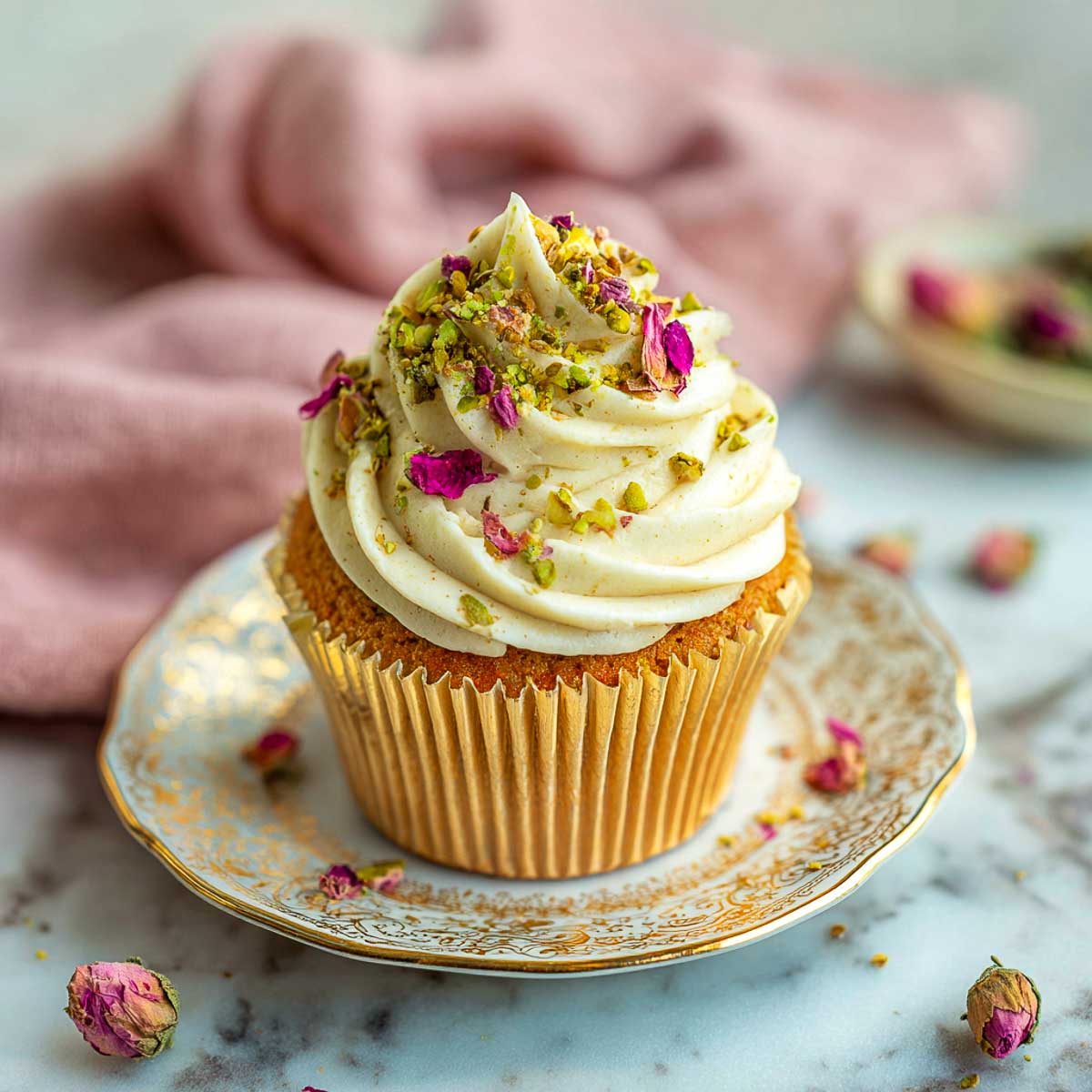 Rose and pistachio cupcakes on ornate platter with frosting and petals.