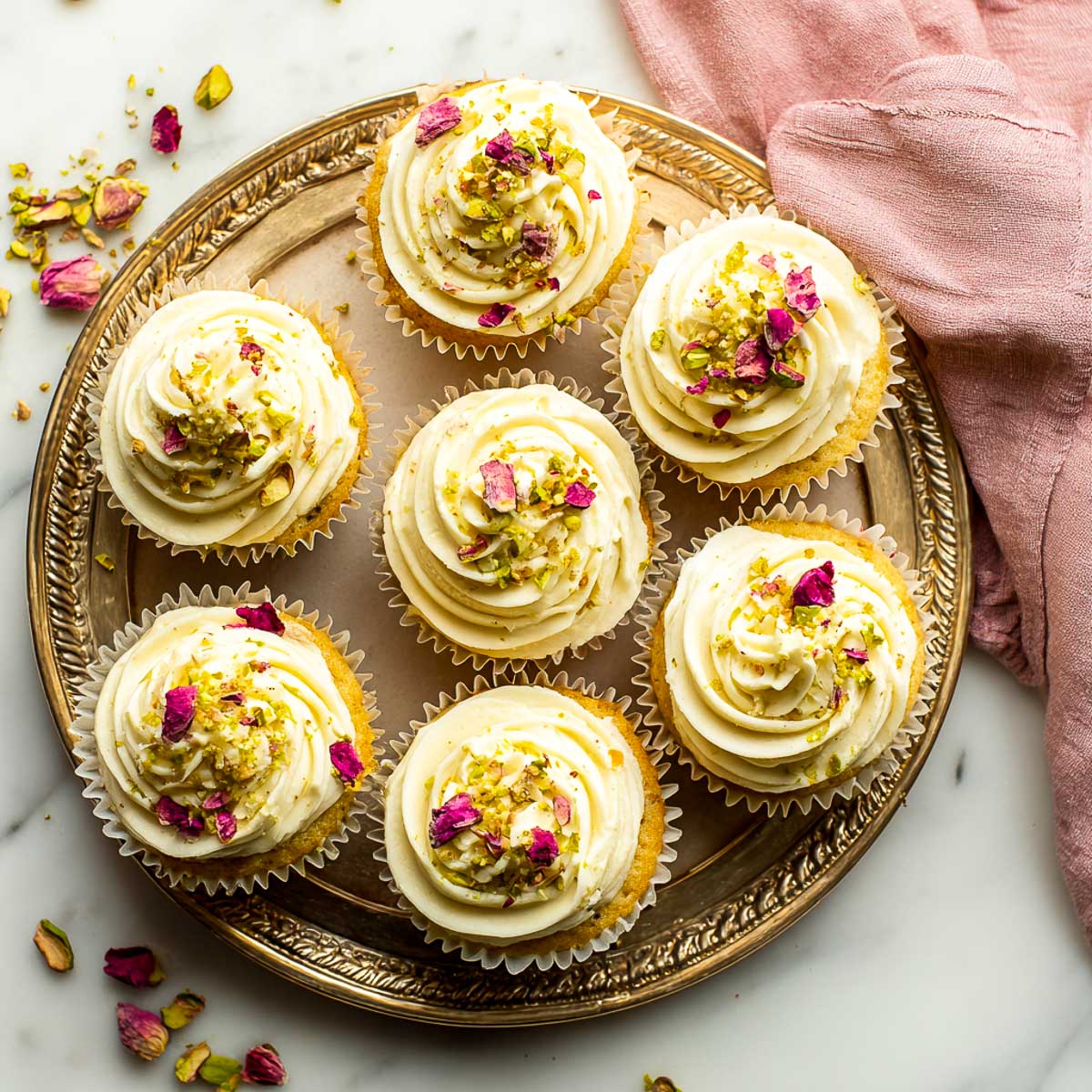 Tray of rose and pistachio cupcakes topped with frosting and floral garnish.