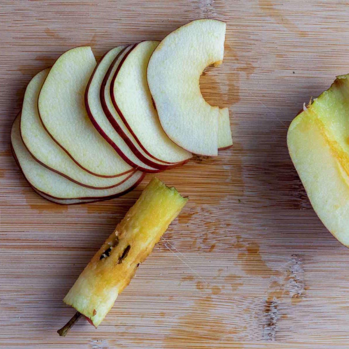 Fresh apple sliced thinly with the core removed on a wooden cutting board.