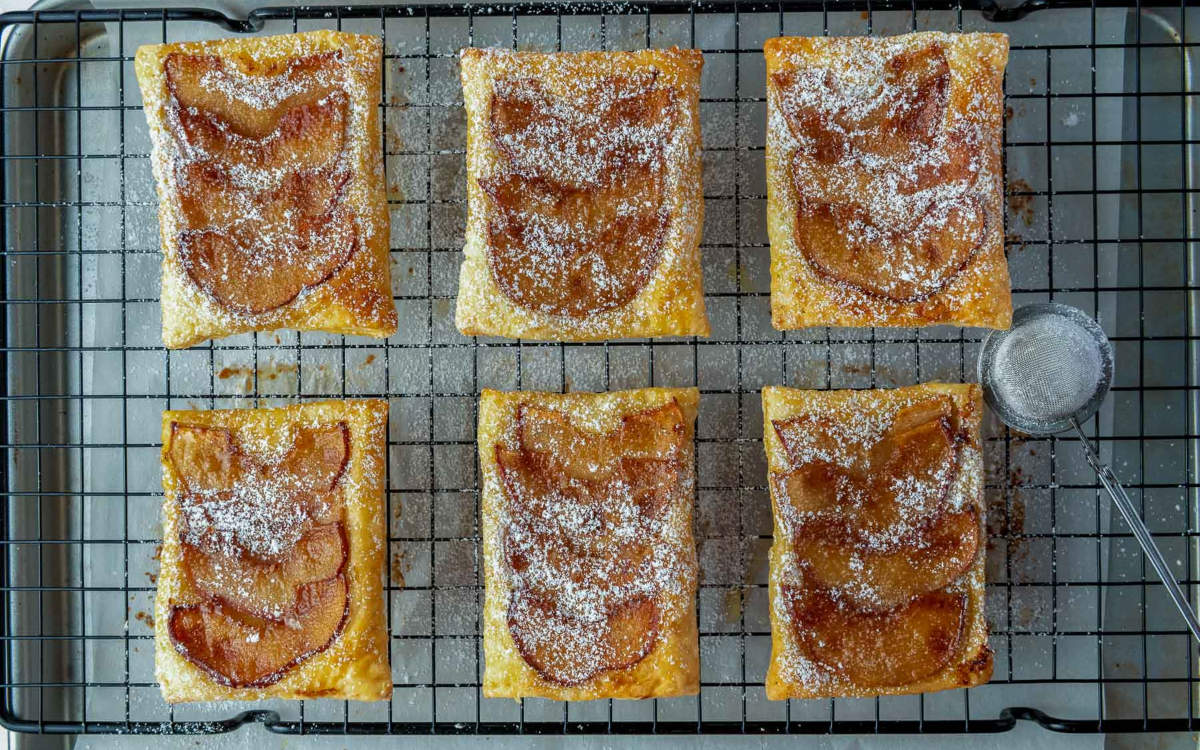 Upside down apple tarts dusted with powdered sugar on a cooling rack.