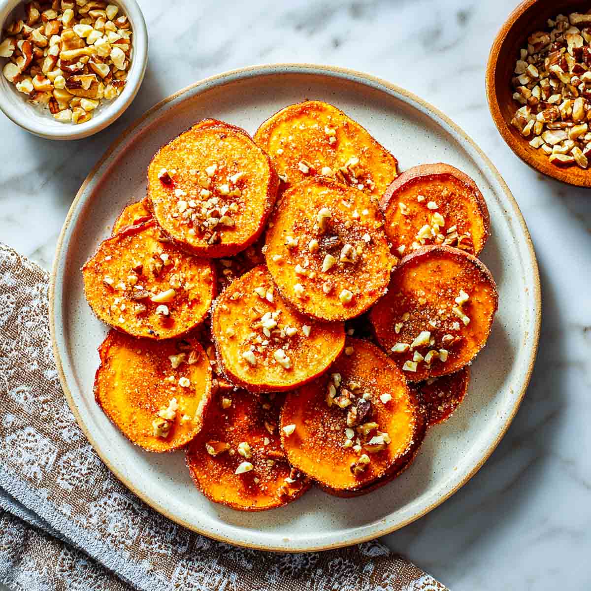 Top-down view of sweet potato slices topped with crushed nuts and cinnamon sugar on a ceramic plate.