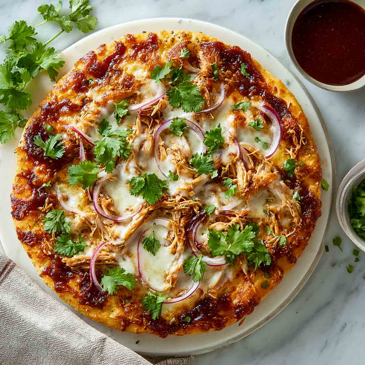 BBQ turkey pizza with melted cheese, red onions, and cilantro on a white pizza stone.