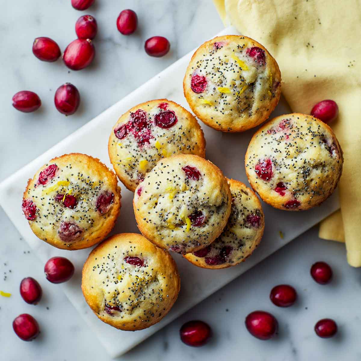 Cranberry lemon muffins with poppy seeds on marble surface.
