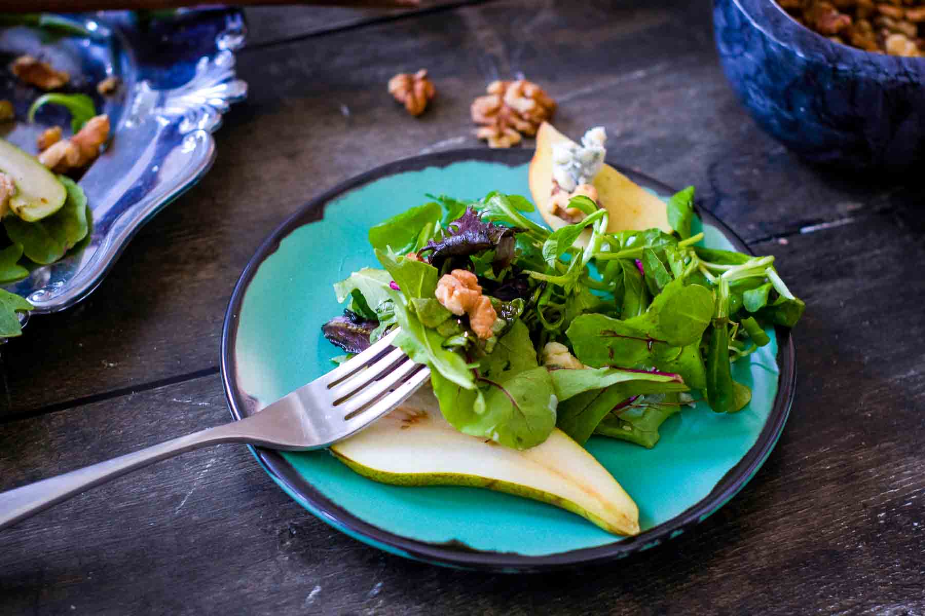 Fresh harvest salad on a turquoise plate with pears, walnuts, and leafy greens.