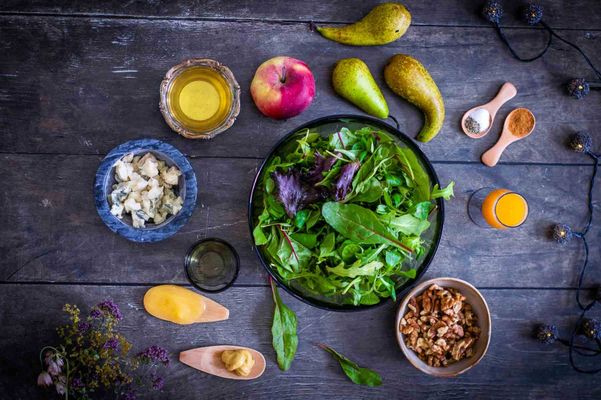 Ingredients for a festive harvest salad, including pears, apples, walnuts, greens, and spices.