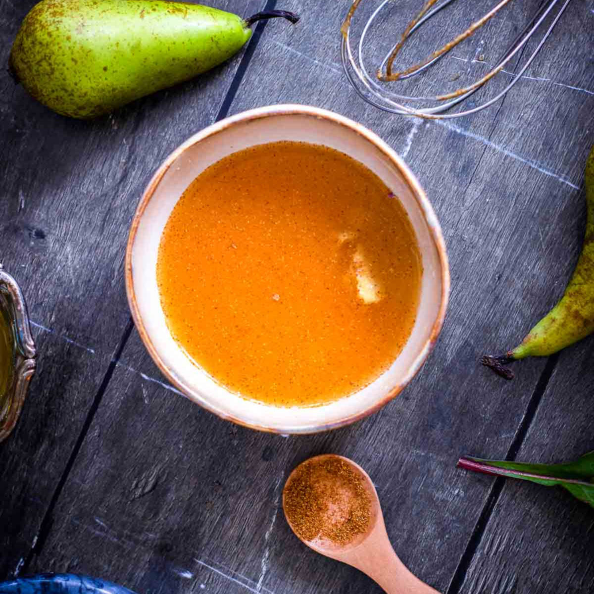 Bowl of spiced vinaigrette dressing for festive harvest salad with whisk on the side.