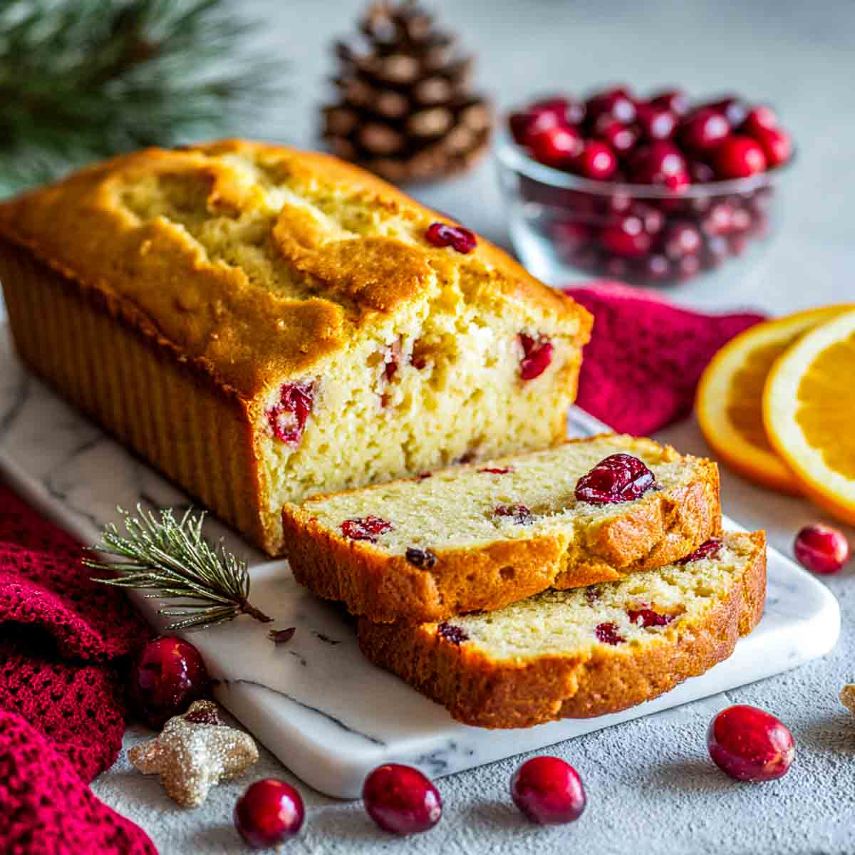 Keto almond flour cranberry orange loaf sliced on a marble board with cranberries and orange slices.