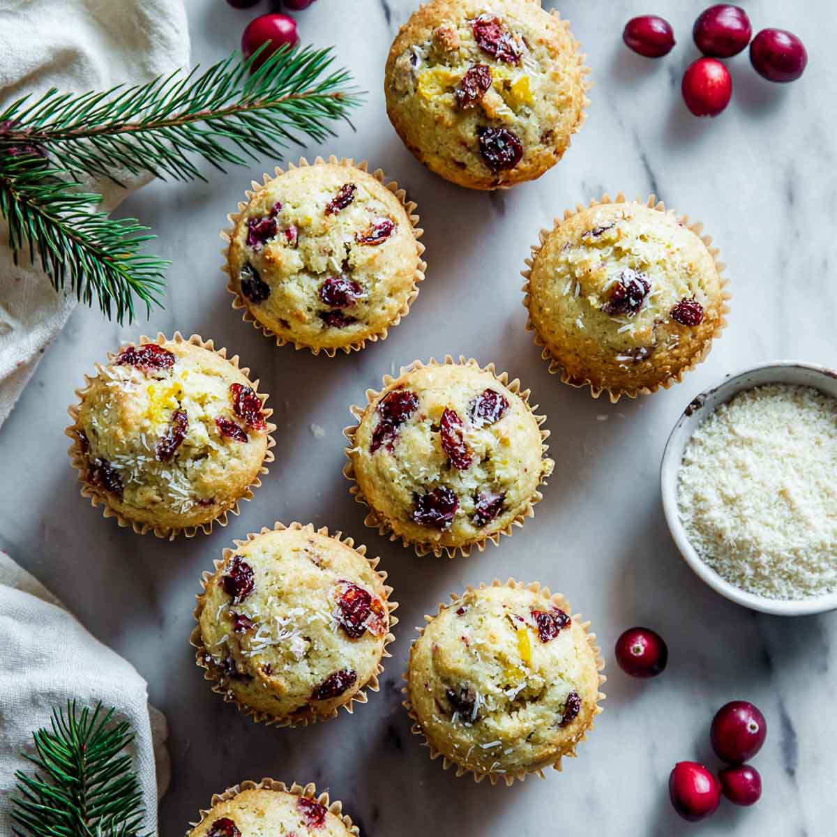Paleo cranberry orange muffins on marble surface with bowl of coconut flour in the background.