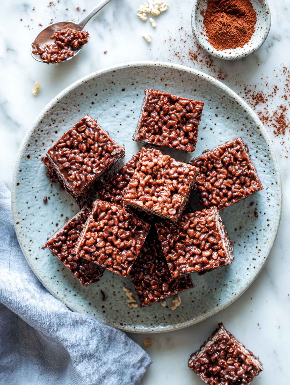 A top-down view of vegan chocolate Rice Krispie treats cut into squares on a speckled plate.