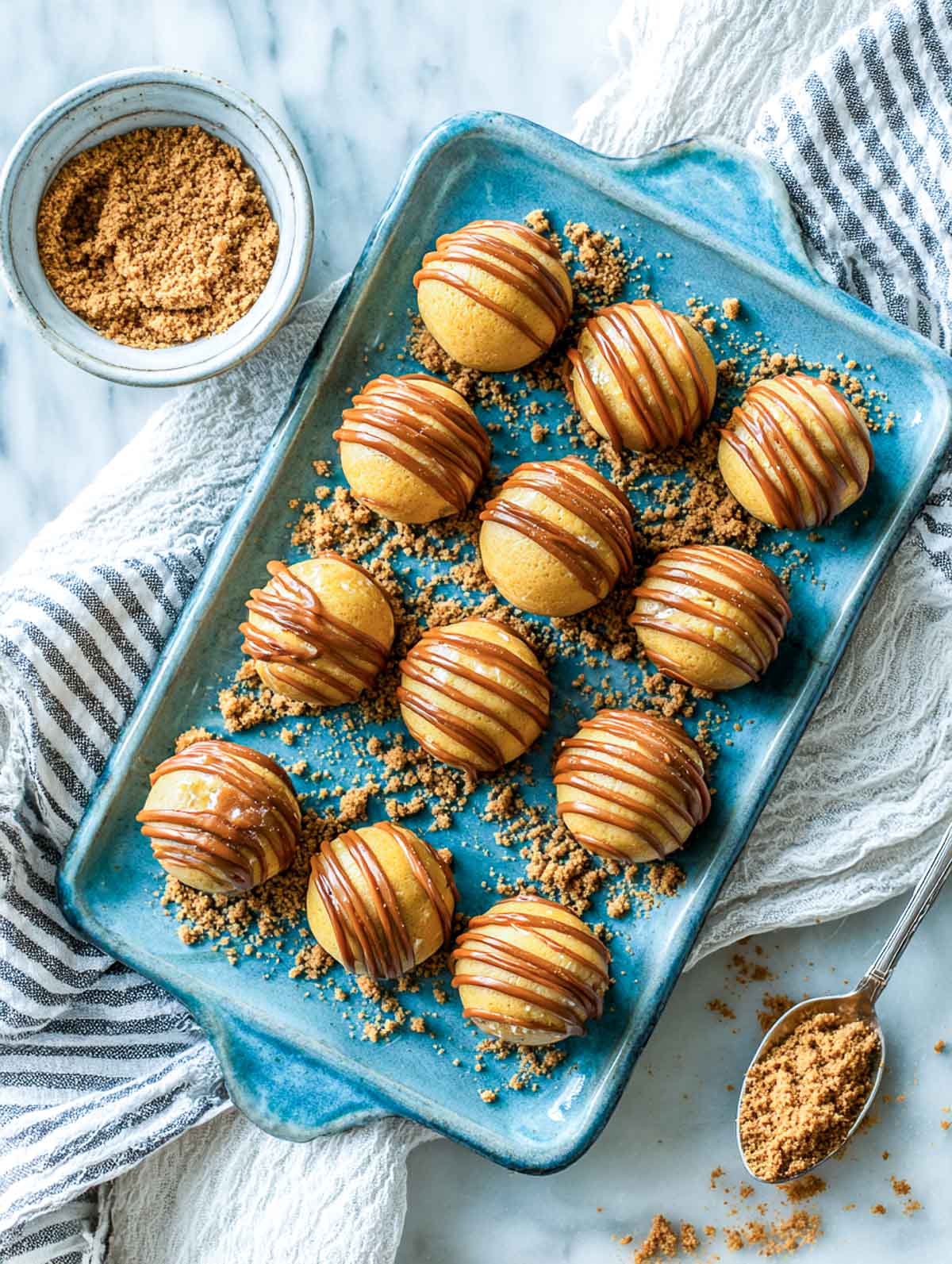 Biscoff truffles on a blue serving plate drizzled with caramel spread and sprinkled with cookie crumbs.