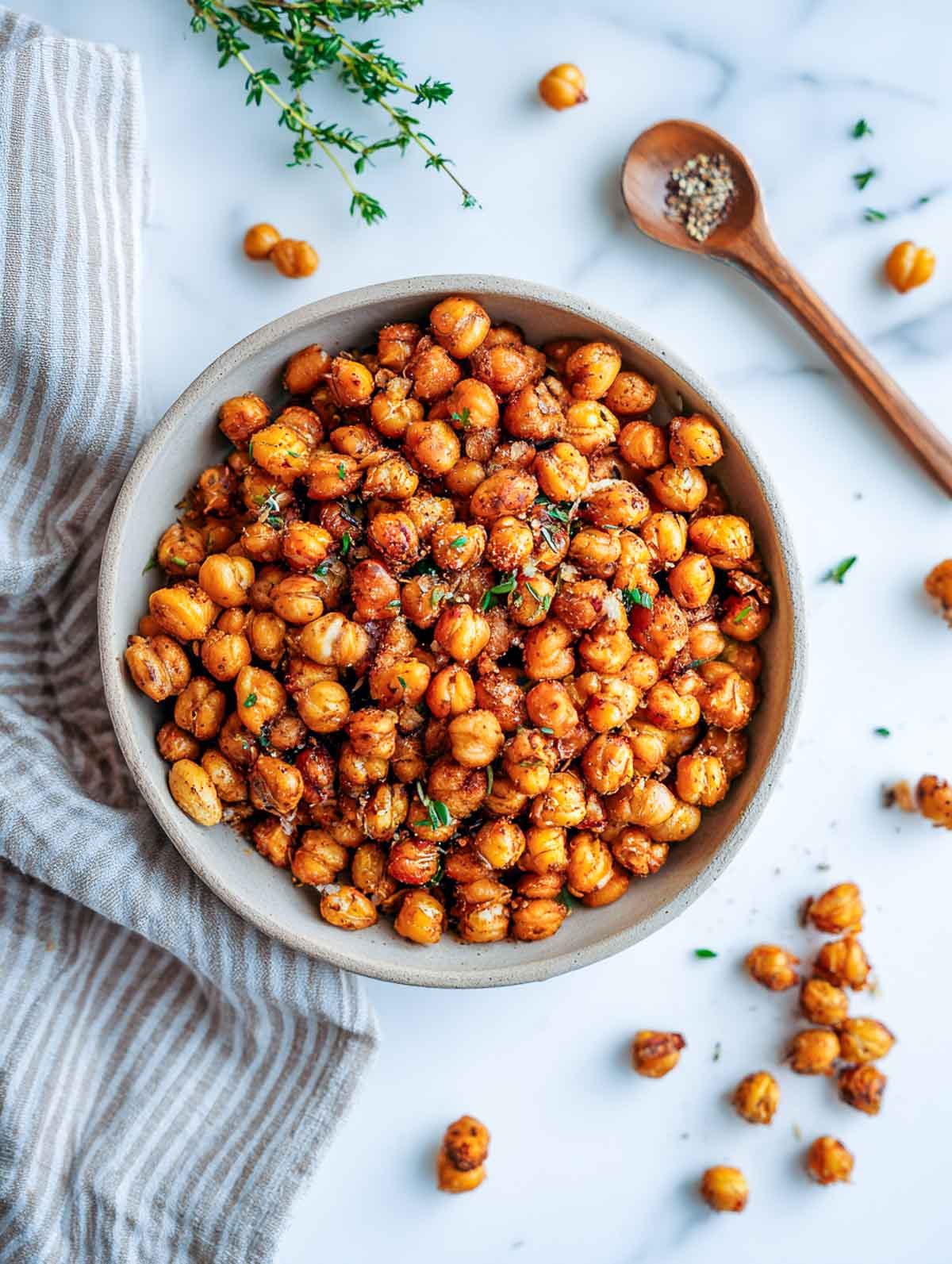 Bowl of roasted chickpea snack mix herbs and spices on a marble counter with a striped napkin.