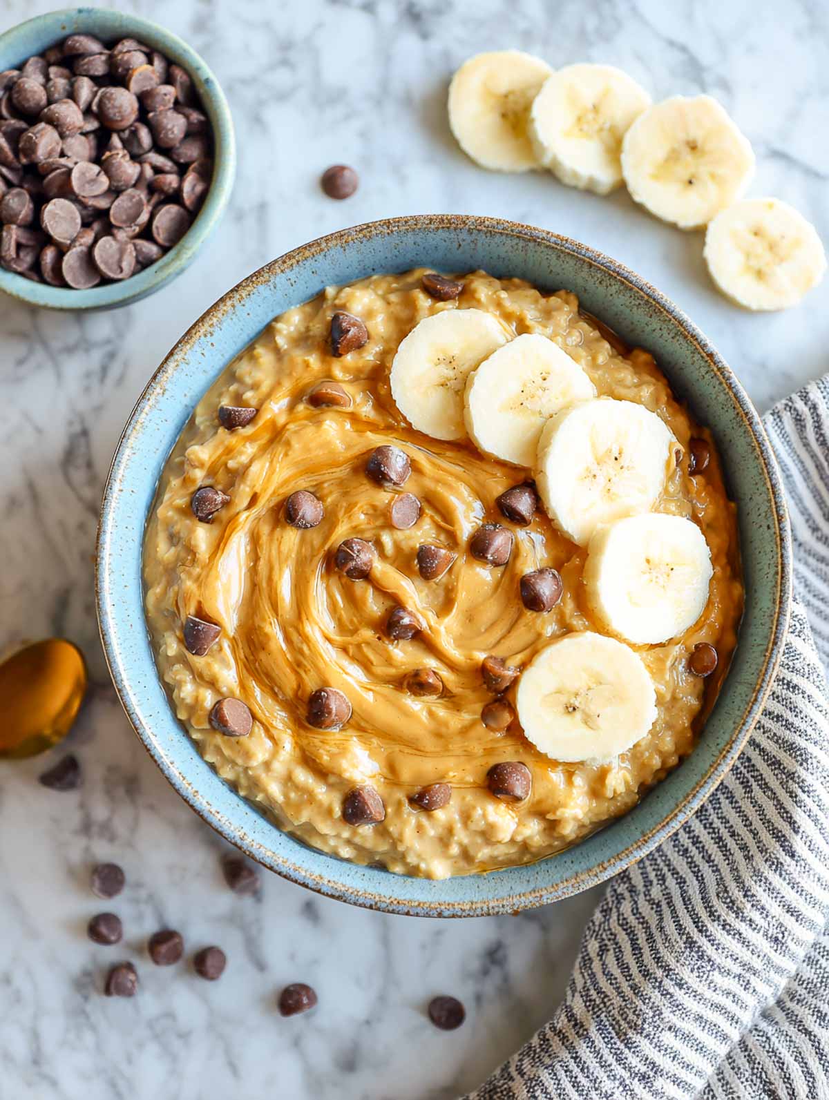 Warm peanut butter banana oatmeal in a muted blue bowl with toppings.