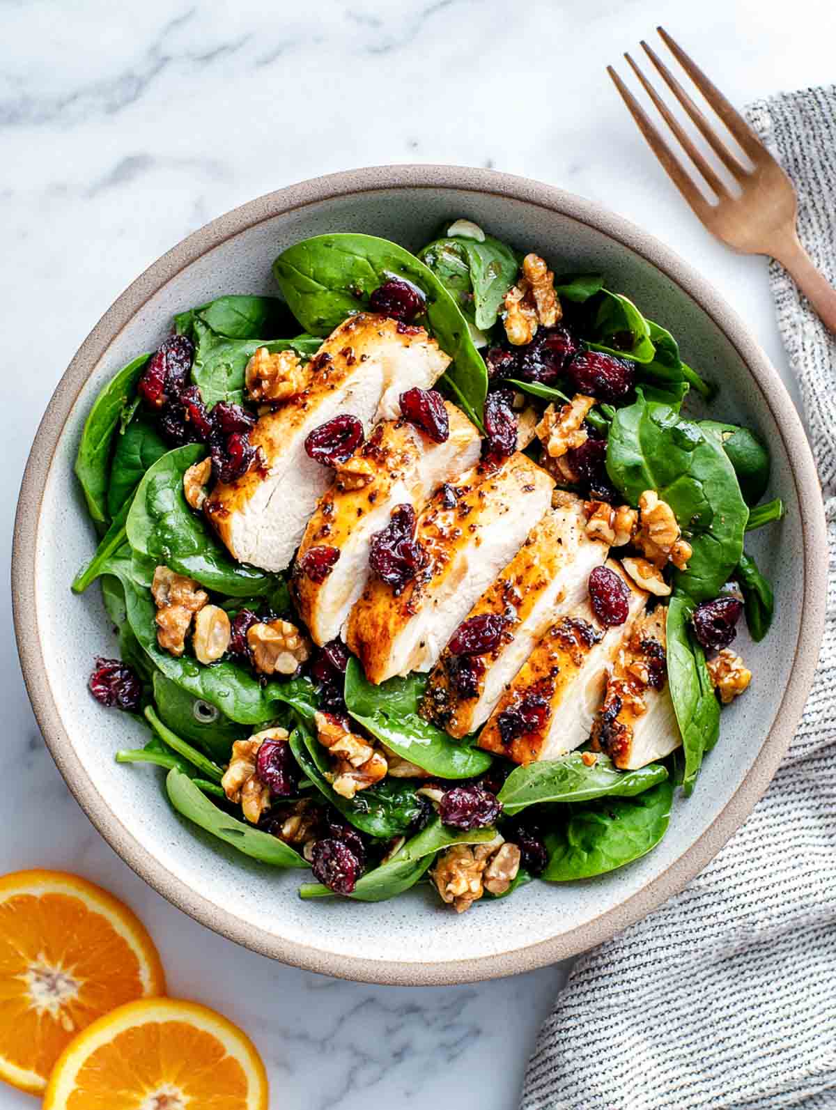 Top-down cranberry spinach winter chicken salad with sliced chicken, cranberries, and walnuts.