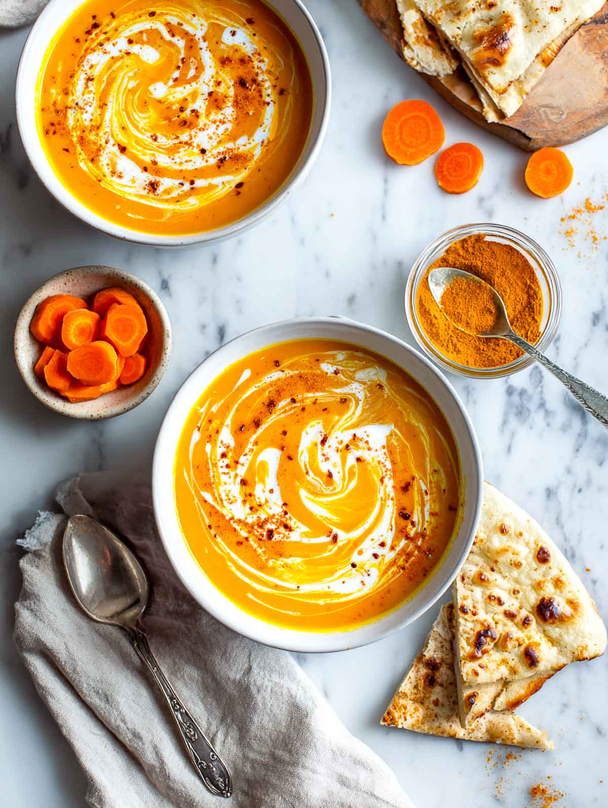 Golden orange sweet potato and carrot soup with a swirl of coconut milk and curry powder, served with naan bread.