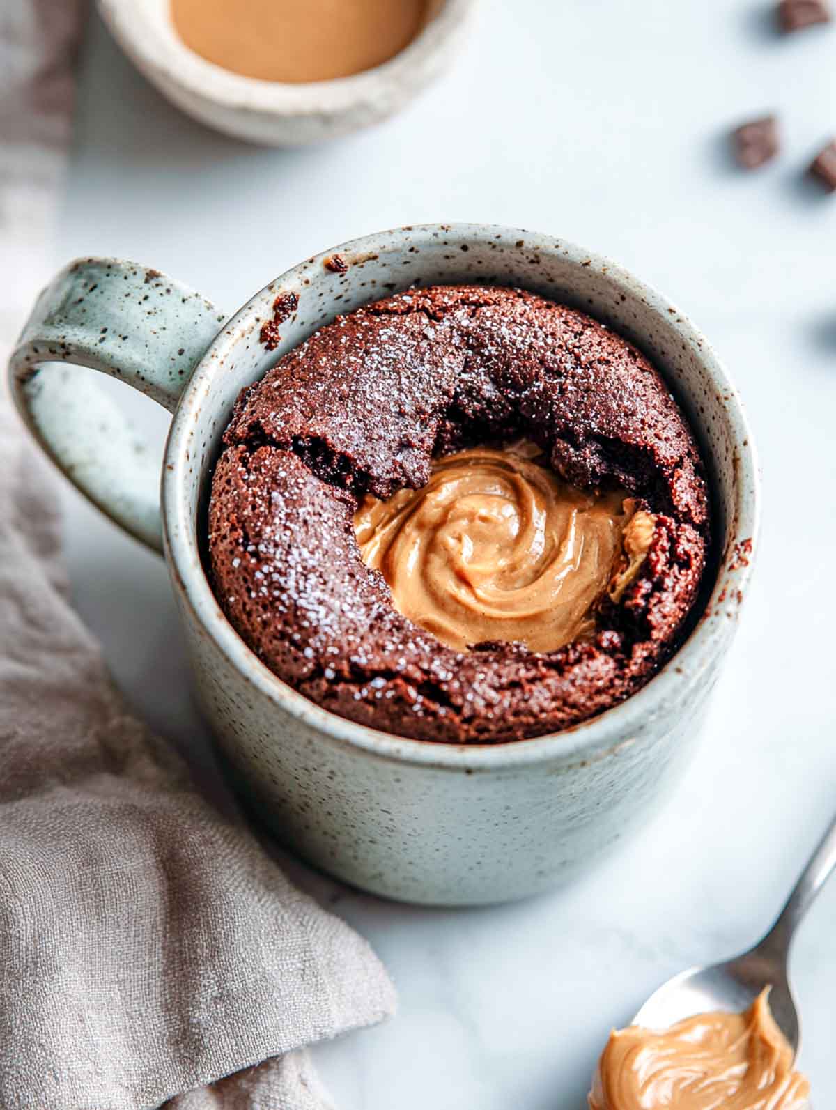 An angled view of a gluten-free chocolate lava cake in a speckled mug with a molten peanut butter center.
