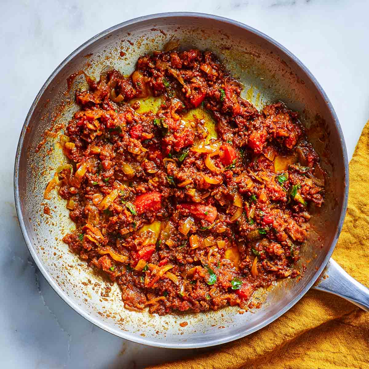 Onion-tomato masala cooking in a stainless steel pan with spices.
