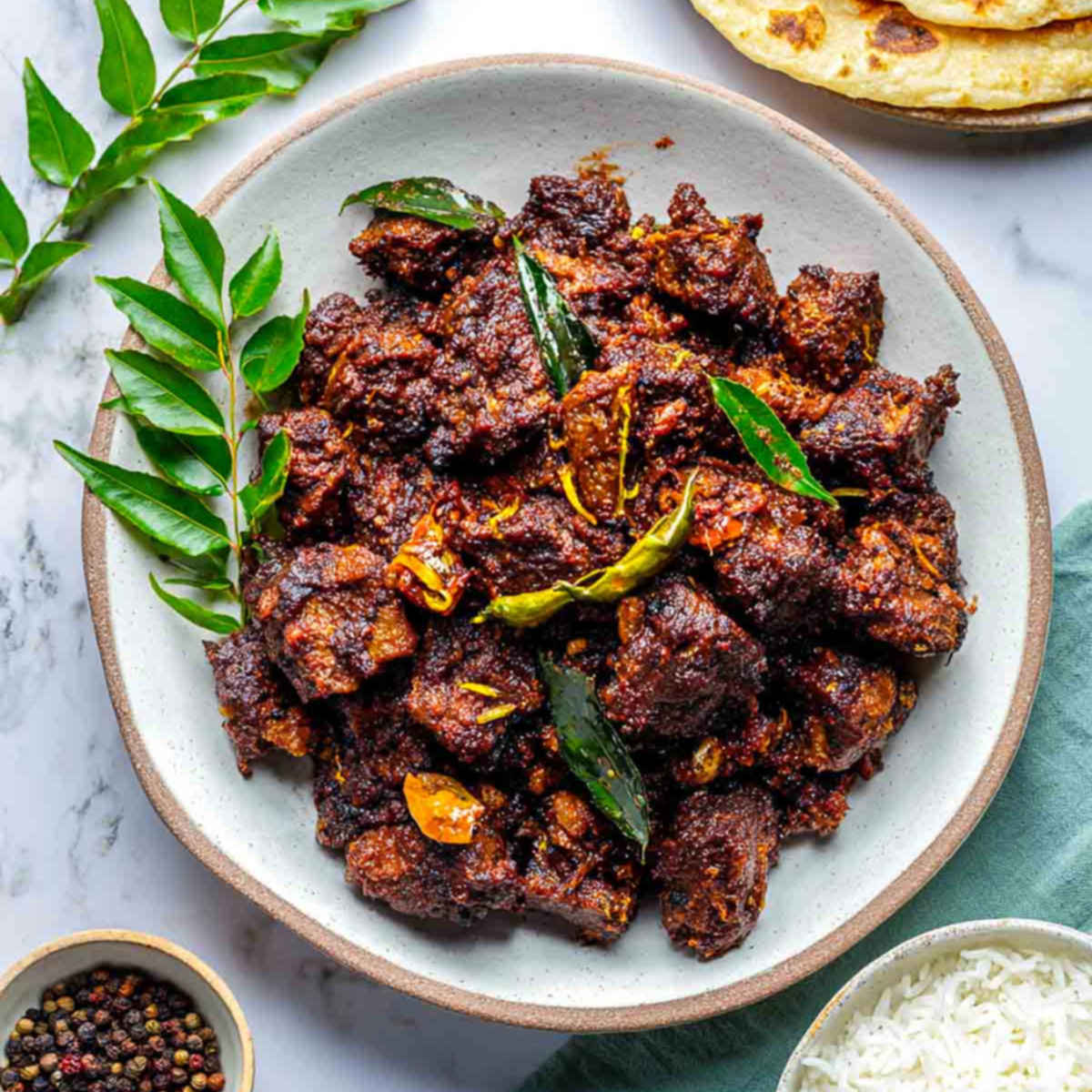 Top view of dark, crispy lamb pepper fry on a plate with rotis.