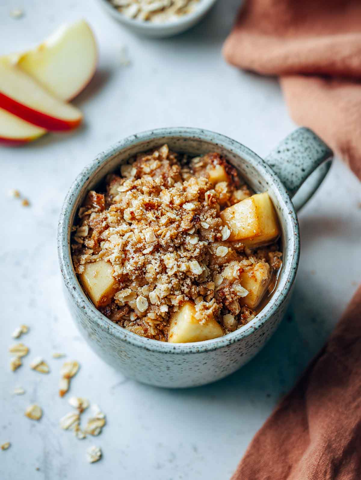 A top-down view of a microwave apple crisp in a speckled mug with tender apple cubes and a golden oat crumble.