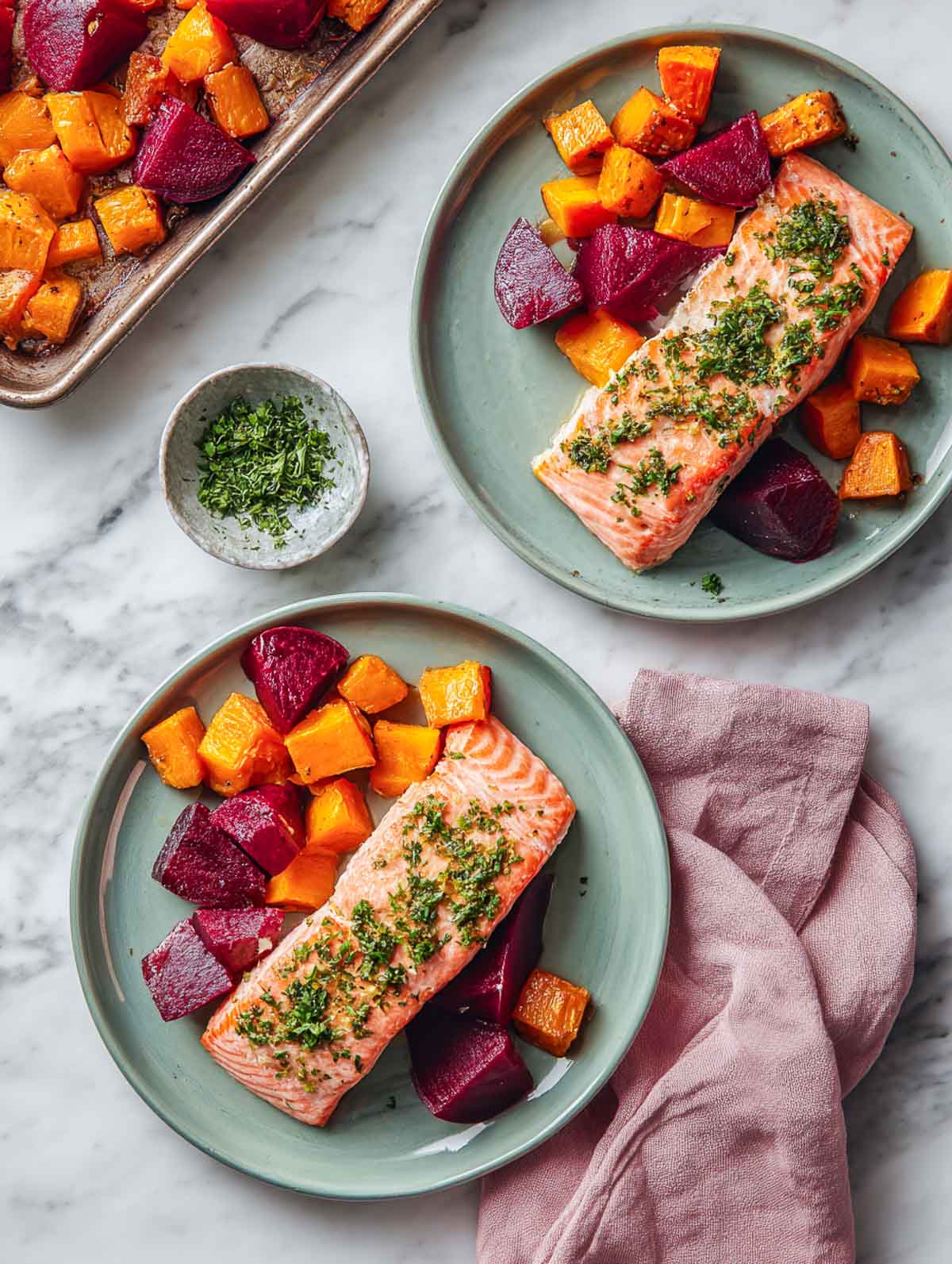Roasted beet and sweet potato salmon fillet on sage plate with herbs.