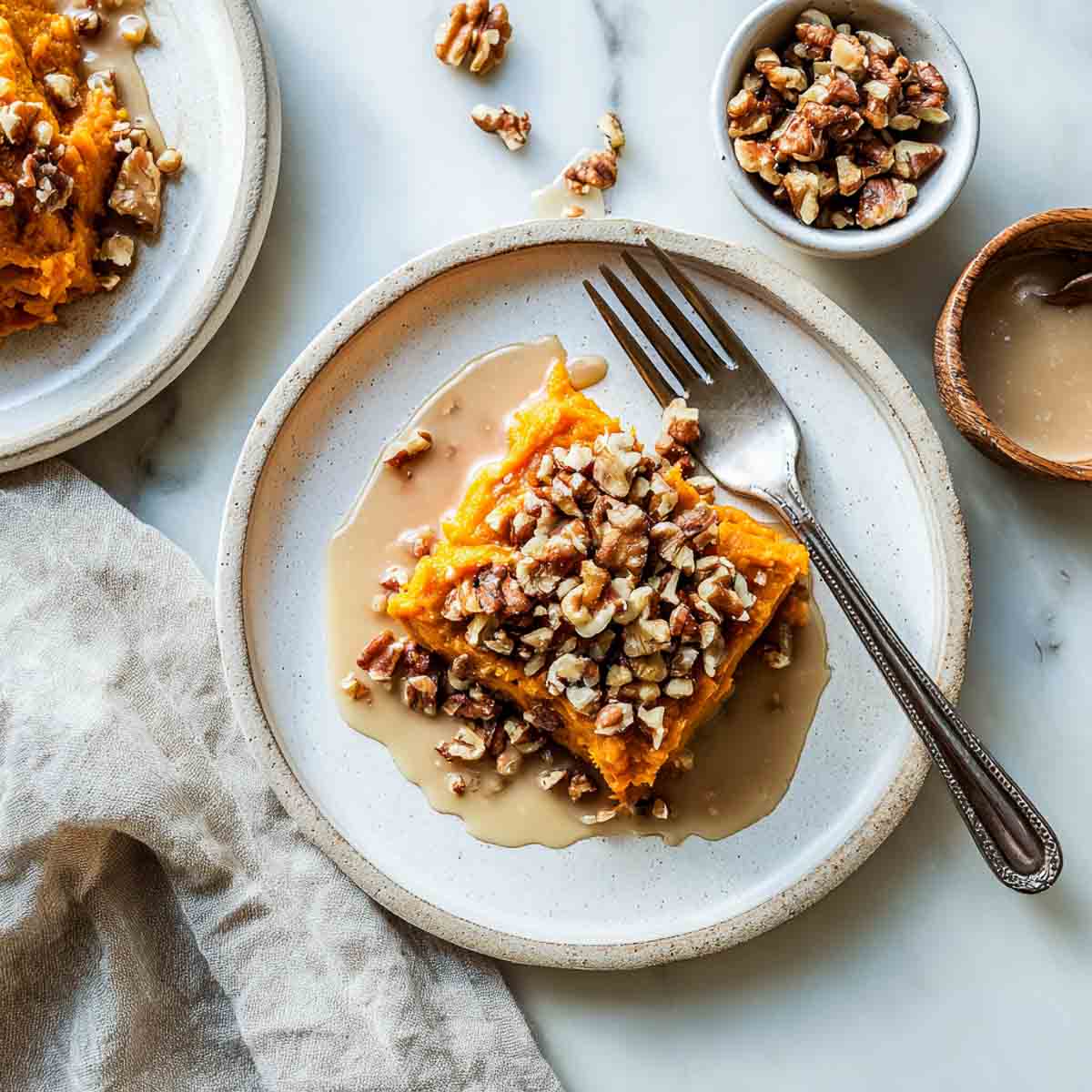 Top-down view of a plated serving of spiced sweet potato casserole with chopped walnuts and a drizzle of ginger glaze on a marble surface.