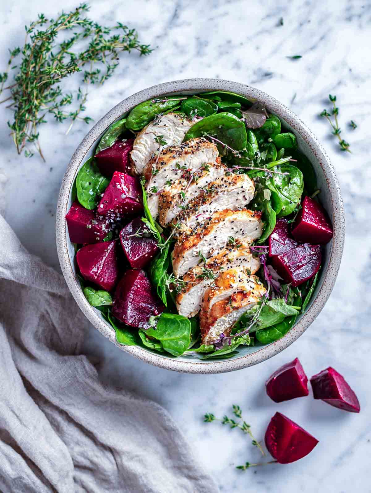Top view of spinach chicken salad with roasted beets and sliced honey-thyme chicken