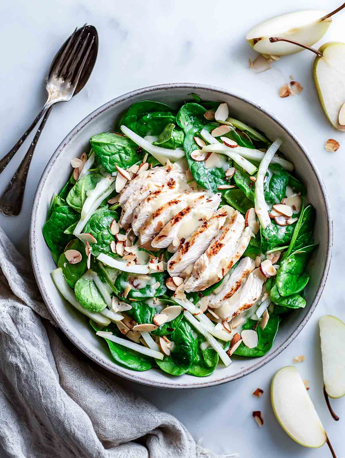 Winter chicken salad with spinach, sliced chicken, pear matchsticks, and almonds in a wide serving bowl.