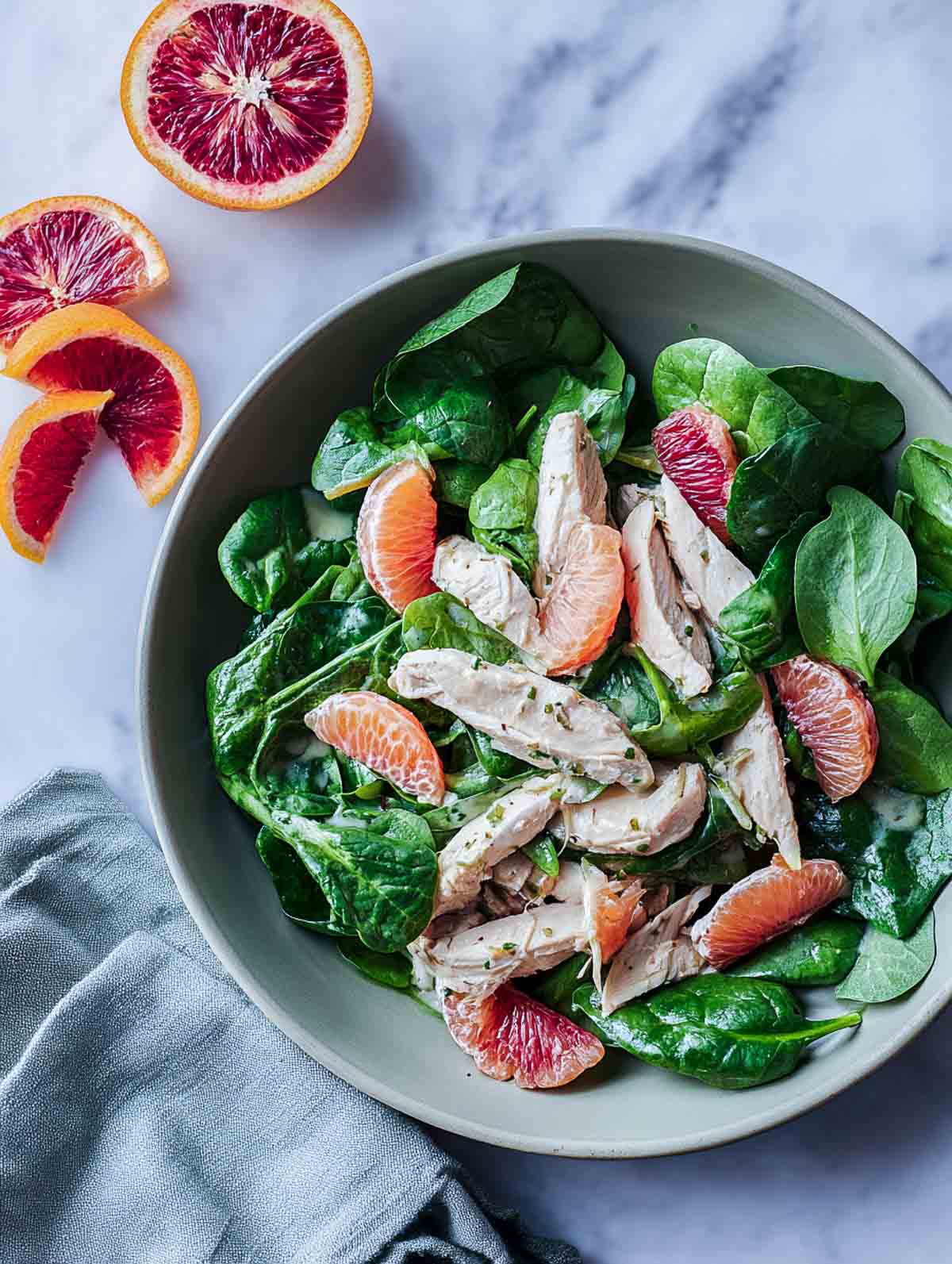 A top-down view of a winter chicken spinach salad topped with sliced chicken breast and bright citrus segments, with a light creamy citrus dressing coating the greens.