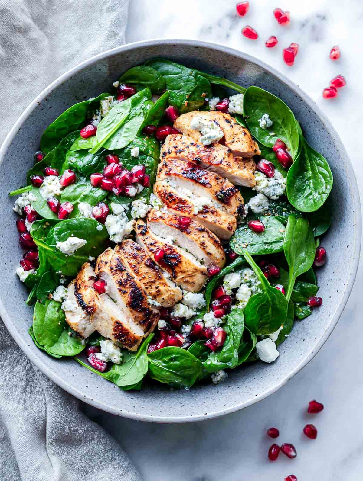 Top view of winter spinach chicken salad with sliced chicken, pomegranate, spinach, and feta.