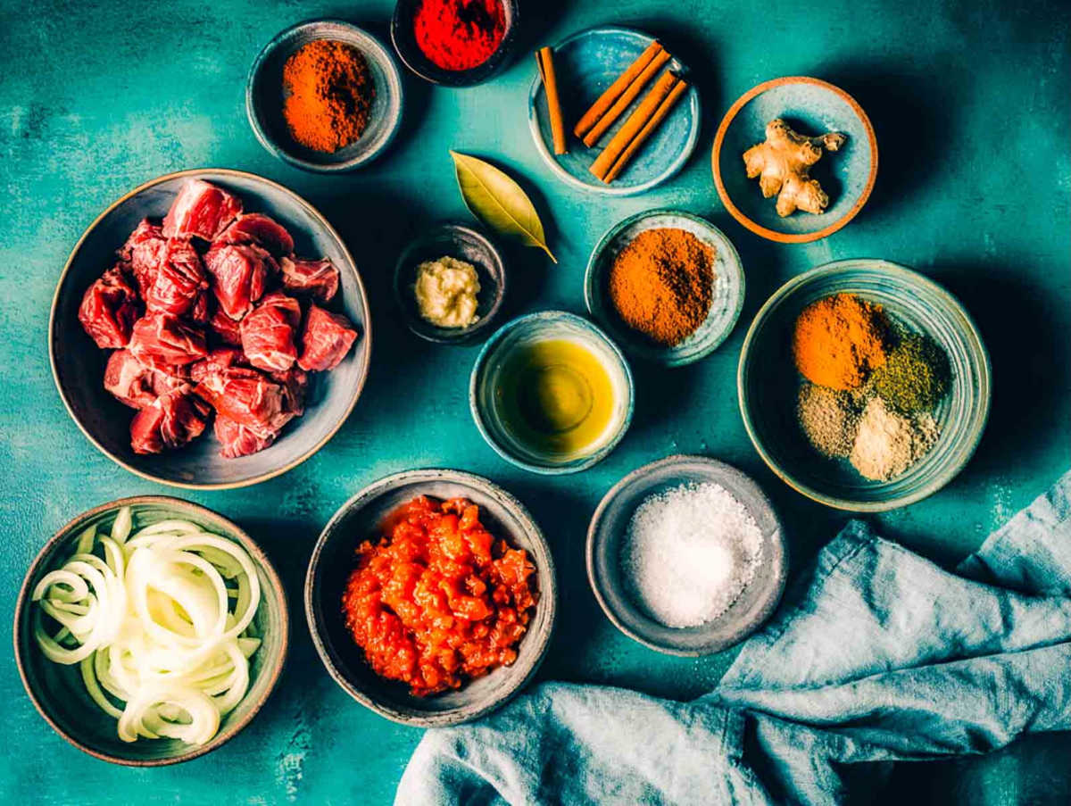 Ingredients for lamb bhuna arranged neatly, including lamb, onions, tomatoes, spices, and oil.
