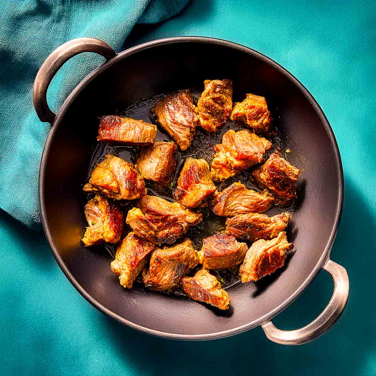 Lamb pieces browning evenly in a wide pan during the initial cooking stage.