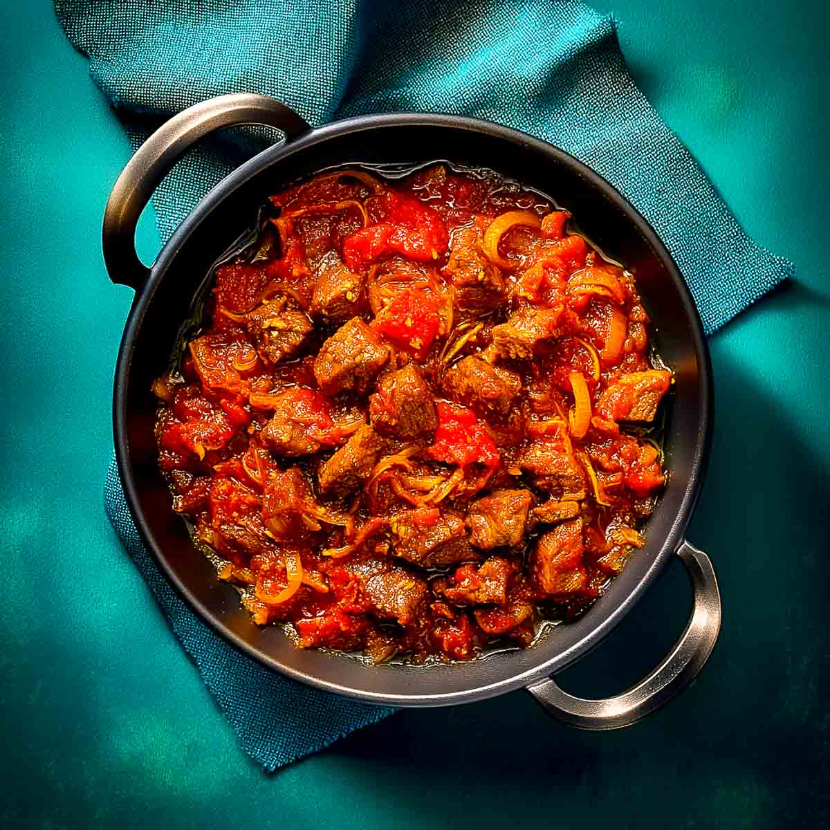 Lamb pieces added to the masala, partially coated and beginning to absorb flavors.