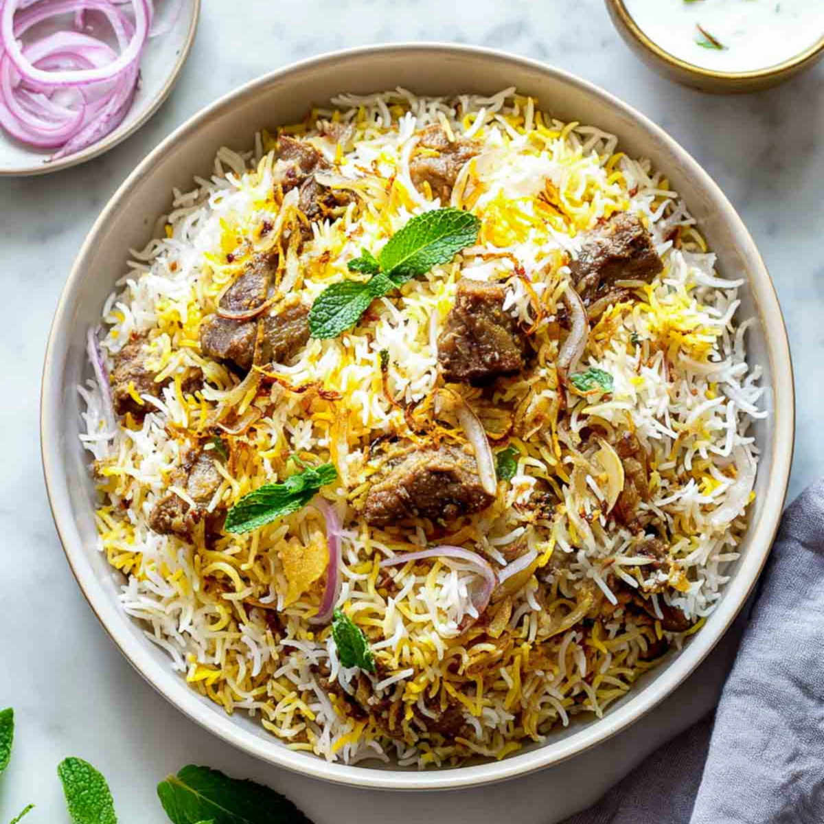 A close view of lamb biryani with saffron rice, onions, and mint.