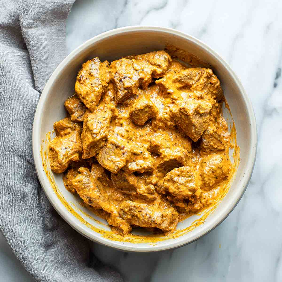 Marinated lamb coated in a thick yogurt spice mixture in a bowl.