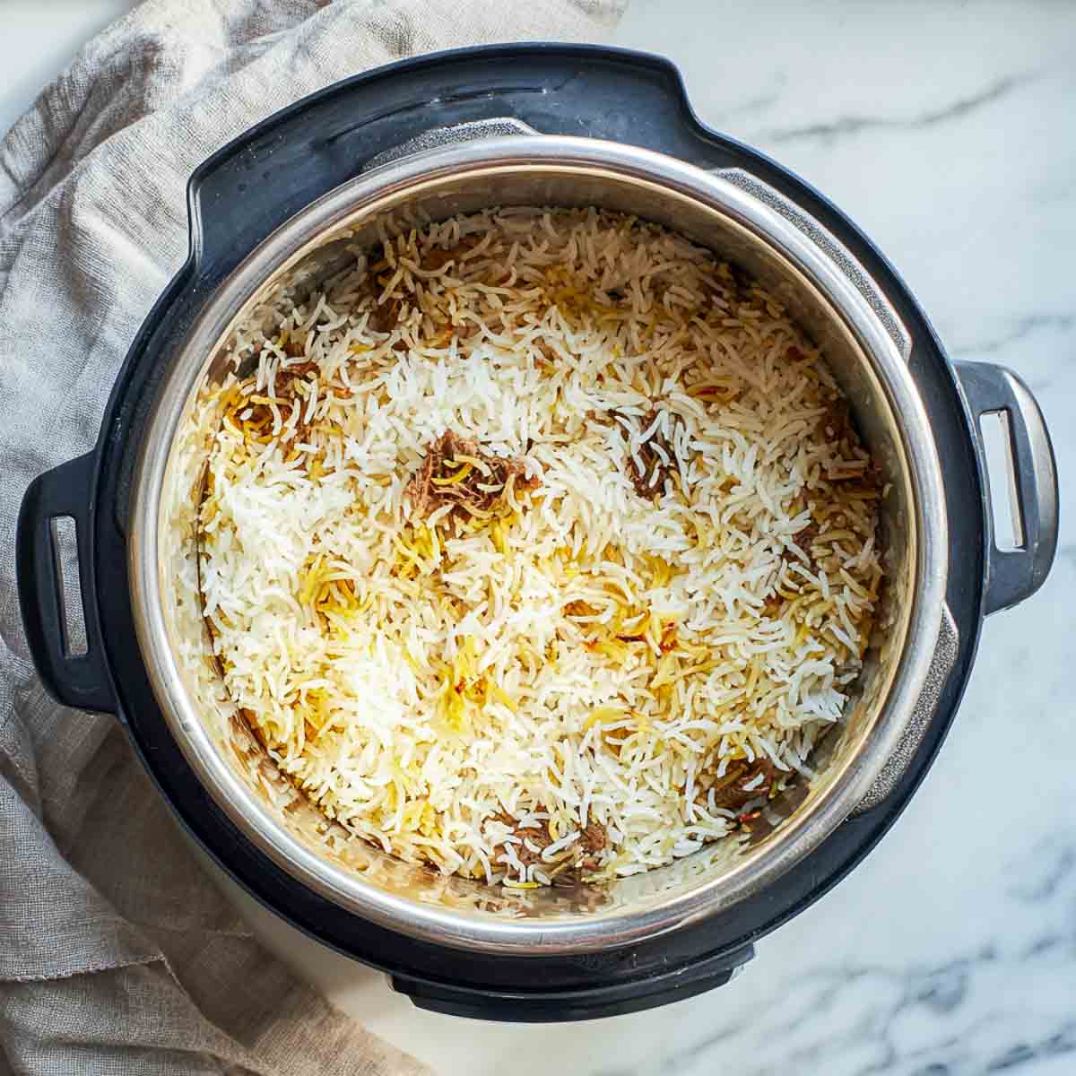Cooked biryani rice resting on top of tender lamb inside the Instant Pot.