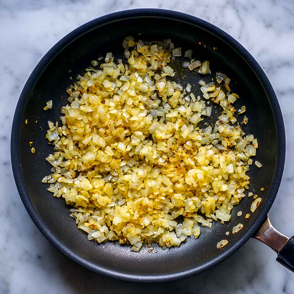Finely chopped onions sautéing in a black pan until soft and lightly golden.