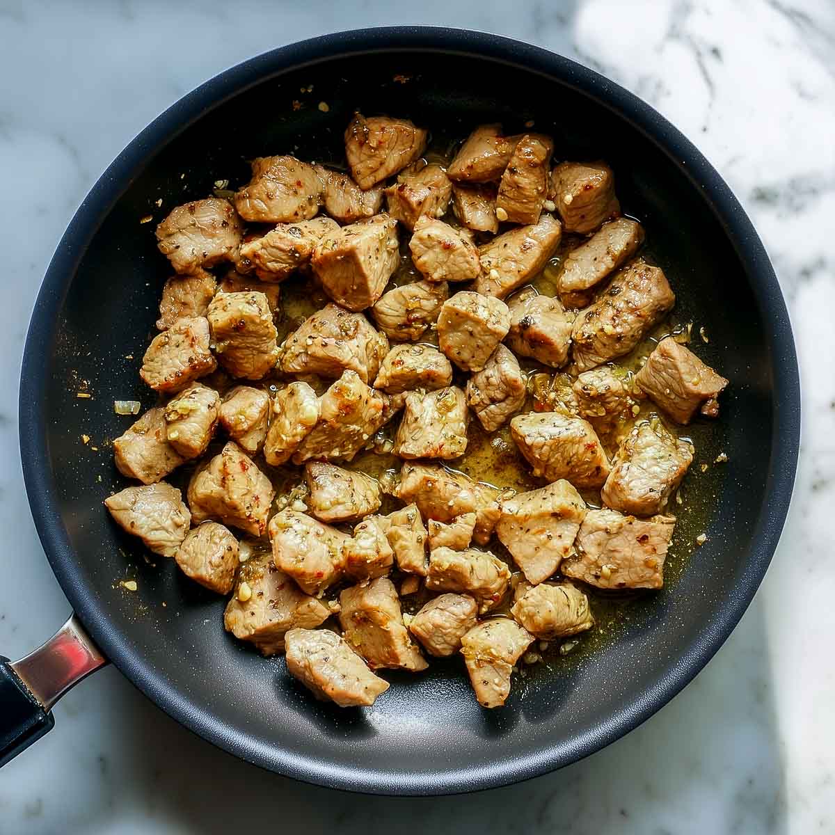Boneless lamb pieces sautéed with ginger garlic paste in oil in a black pan.