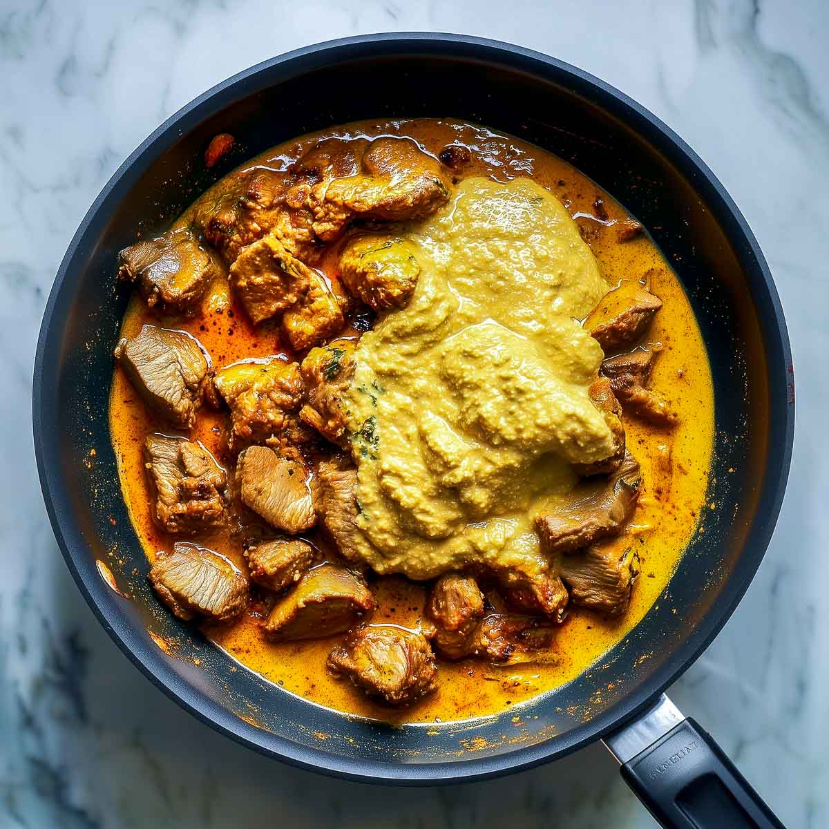 Smooth onion paste added to lamb curry, thickening the korma sauce in the pan.