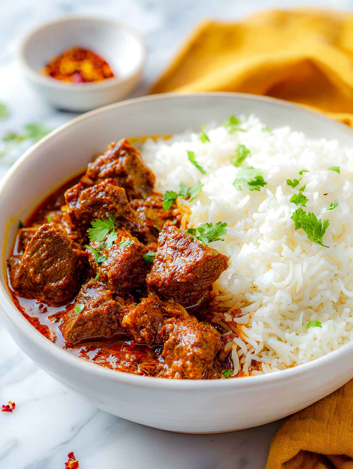 This image shows a bowl of Lamb Madras served with basmati rice, highlighting the tender lamb pieces and vibrant red curry with a sprinkle of fresh cilantro.
