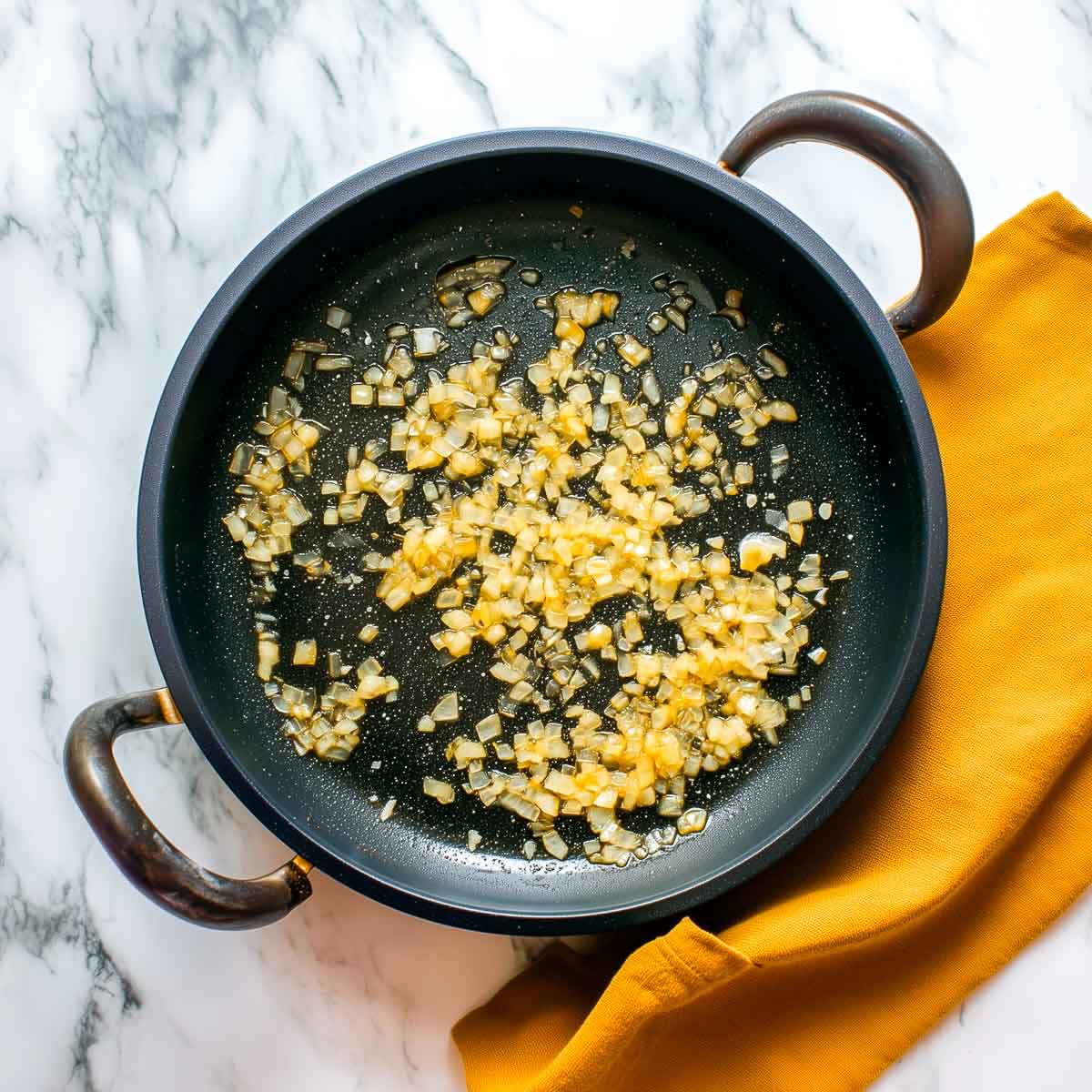This image shows onions sautéing in a black pan as the first step in making Lamb Madras, with softened edges and a light golden color.