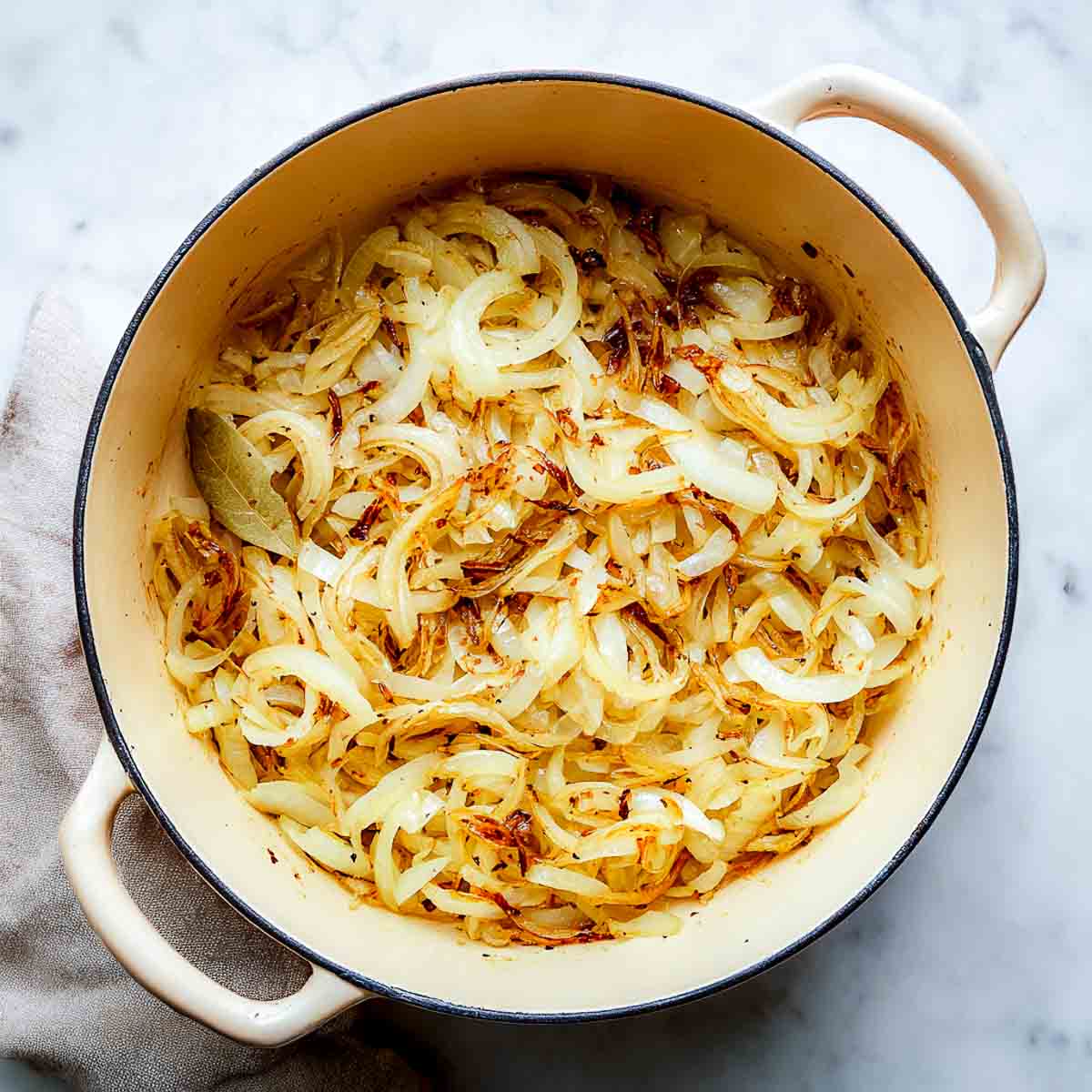 Thinly sliced onions cooking in a cream Dutch oven until soft and lightly golden.