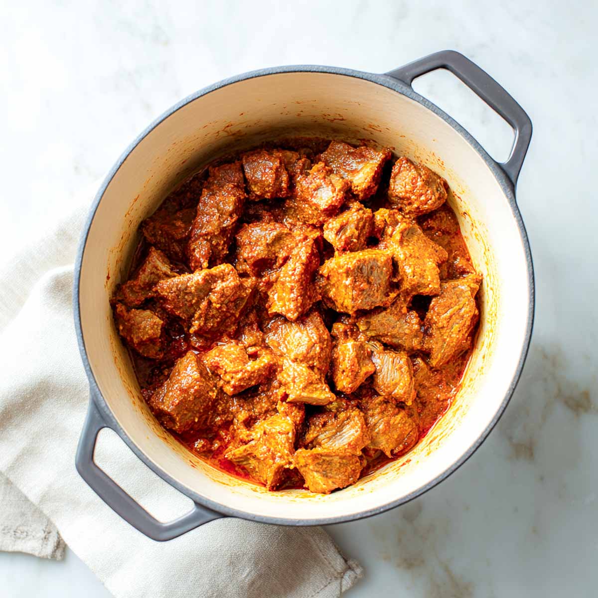 The browned lamb is coated in a thick, vibrant red spice paste inside the Dutch oven.