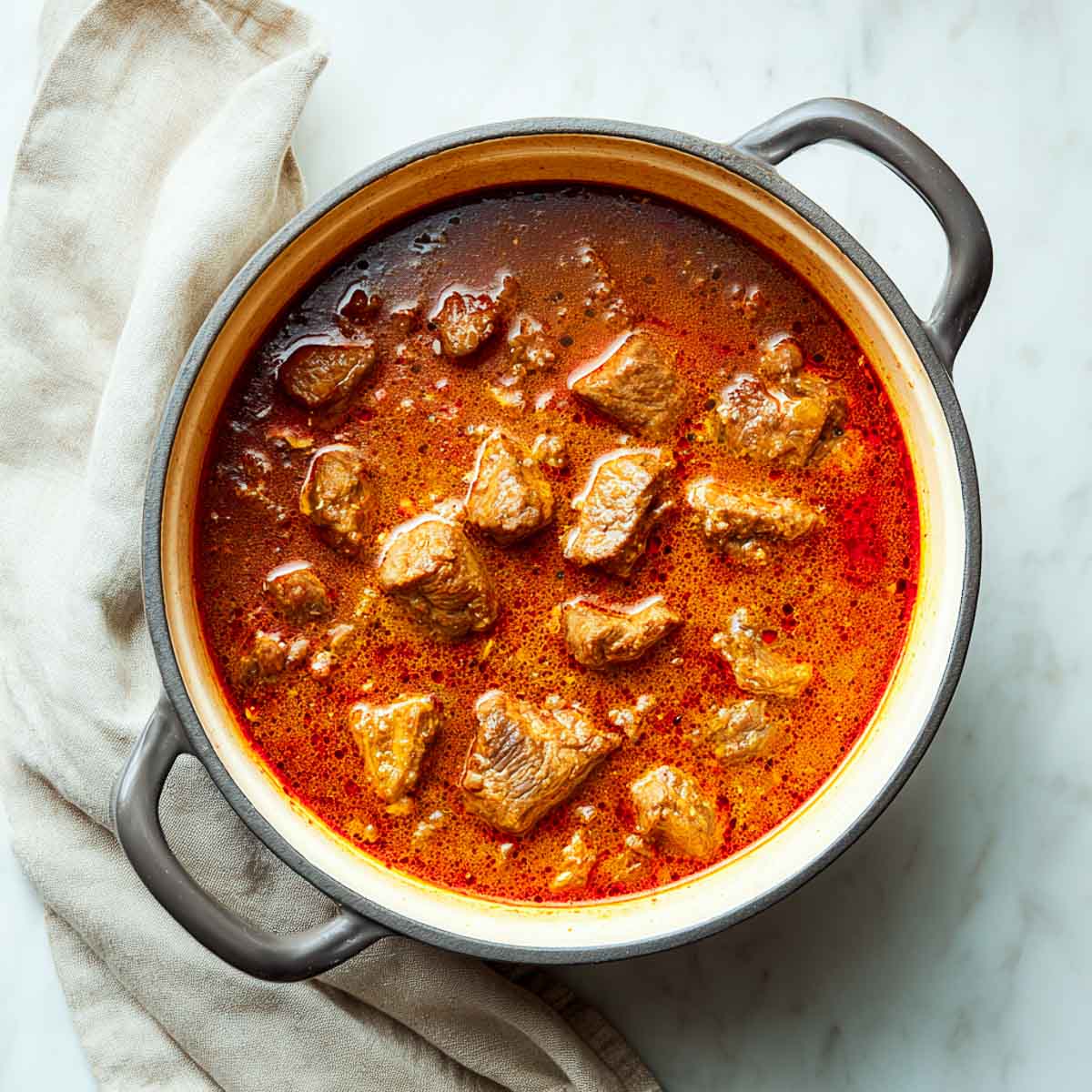 The lamb has been simmered in the sauce until tender, creating a deep red gravy inside the Dutch oven.