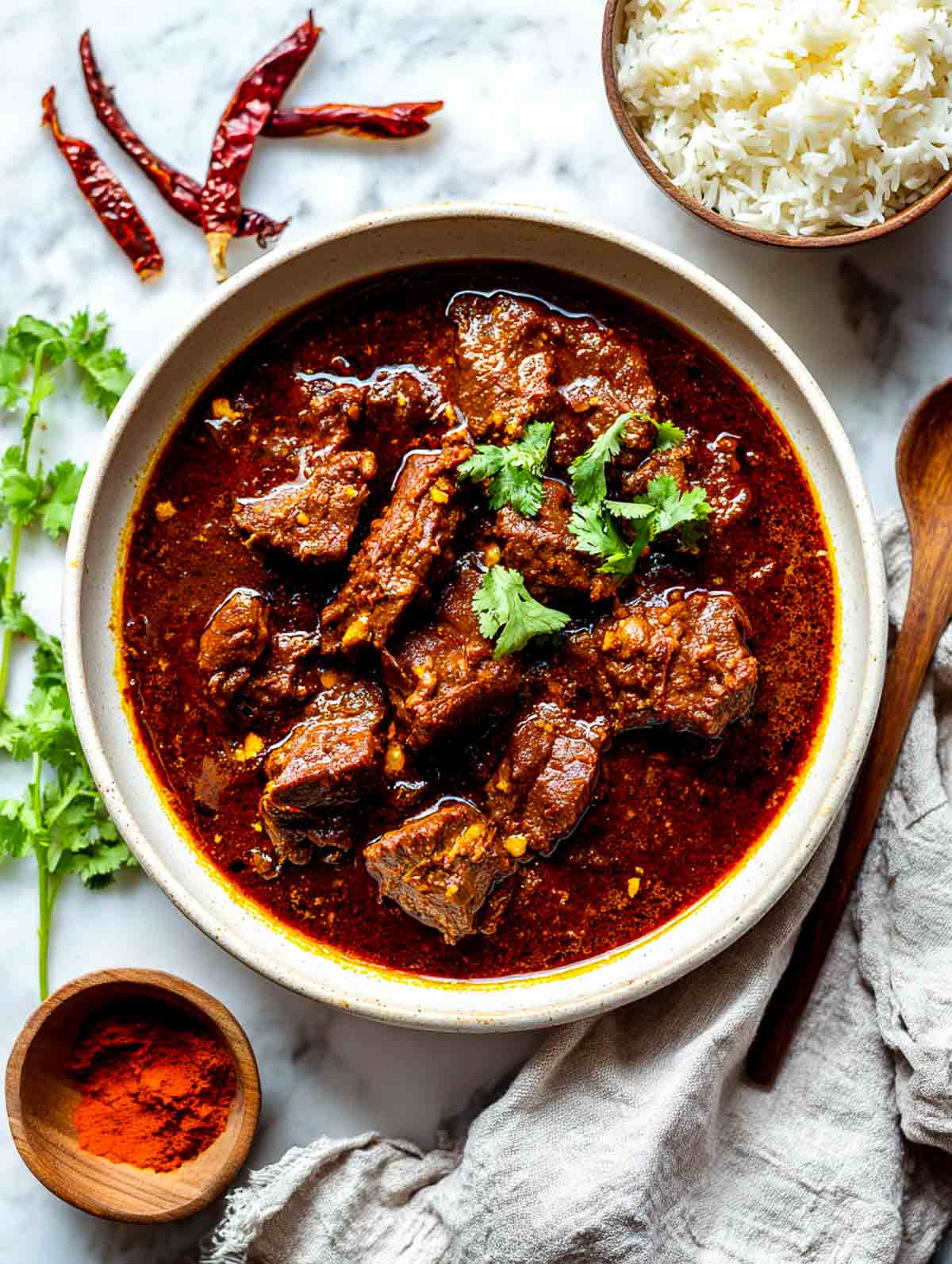 Top down view of lamb vindaloo in a ceramic bowl with rich red curry sauce.