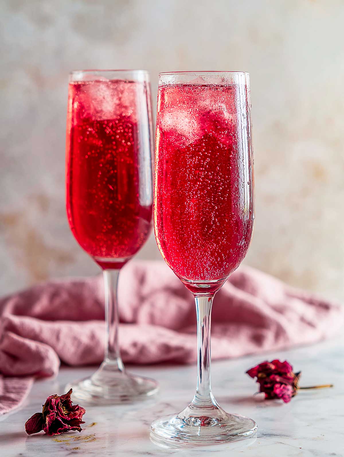 Side view of two sparkling hibiscus vodka spritz cocktails in tall glasses on a white marble surface.