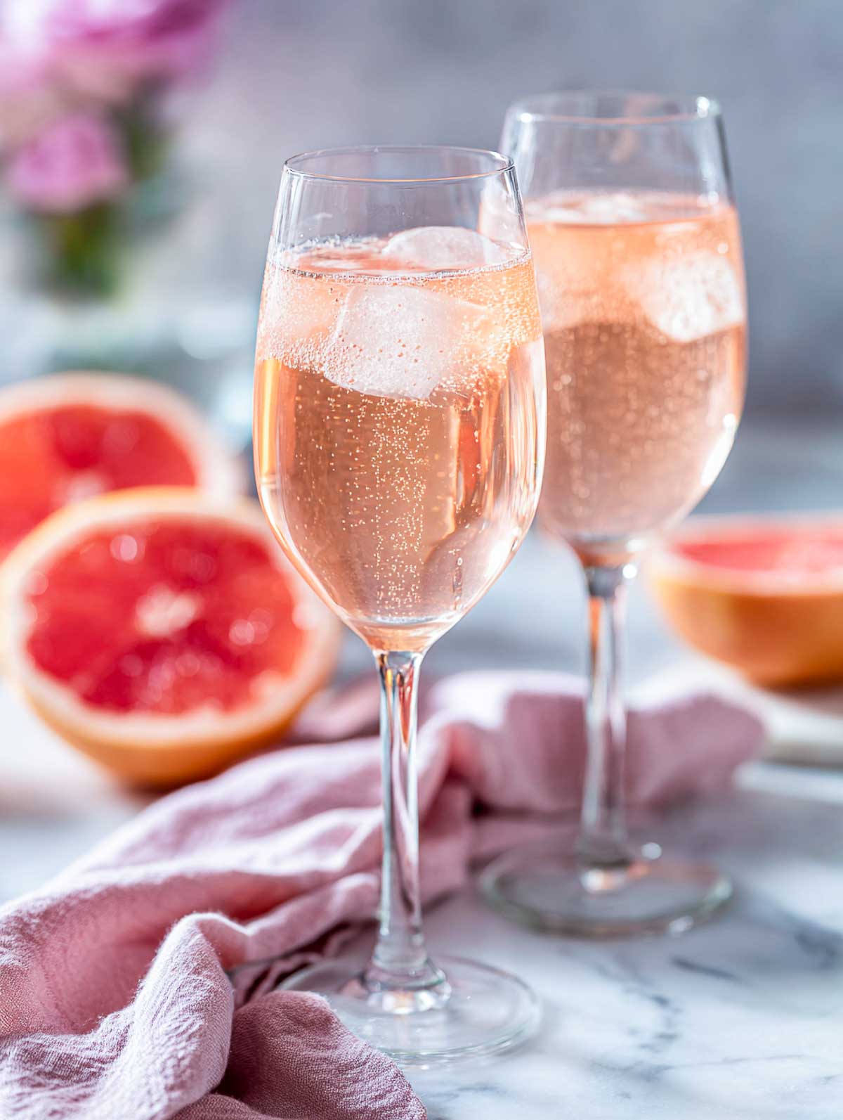 Side view of two sparkling rosé palomas in wine glasses on a white marble surface.