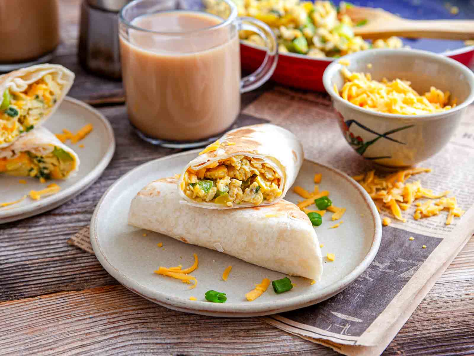Breakfast burritos lined up on board with coffee and scrambled egg filling.